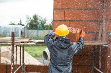 Home Worker with hard hat arranging bricks on a rainy construction site outdoors.