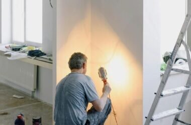 Home Back view of anonymous male in dirty clothes renovating walls in home while holding lamp